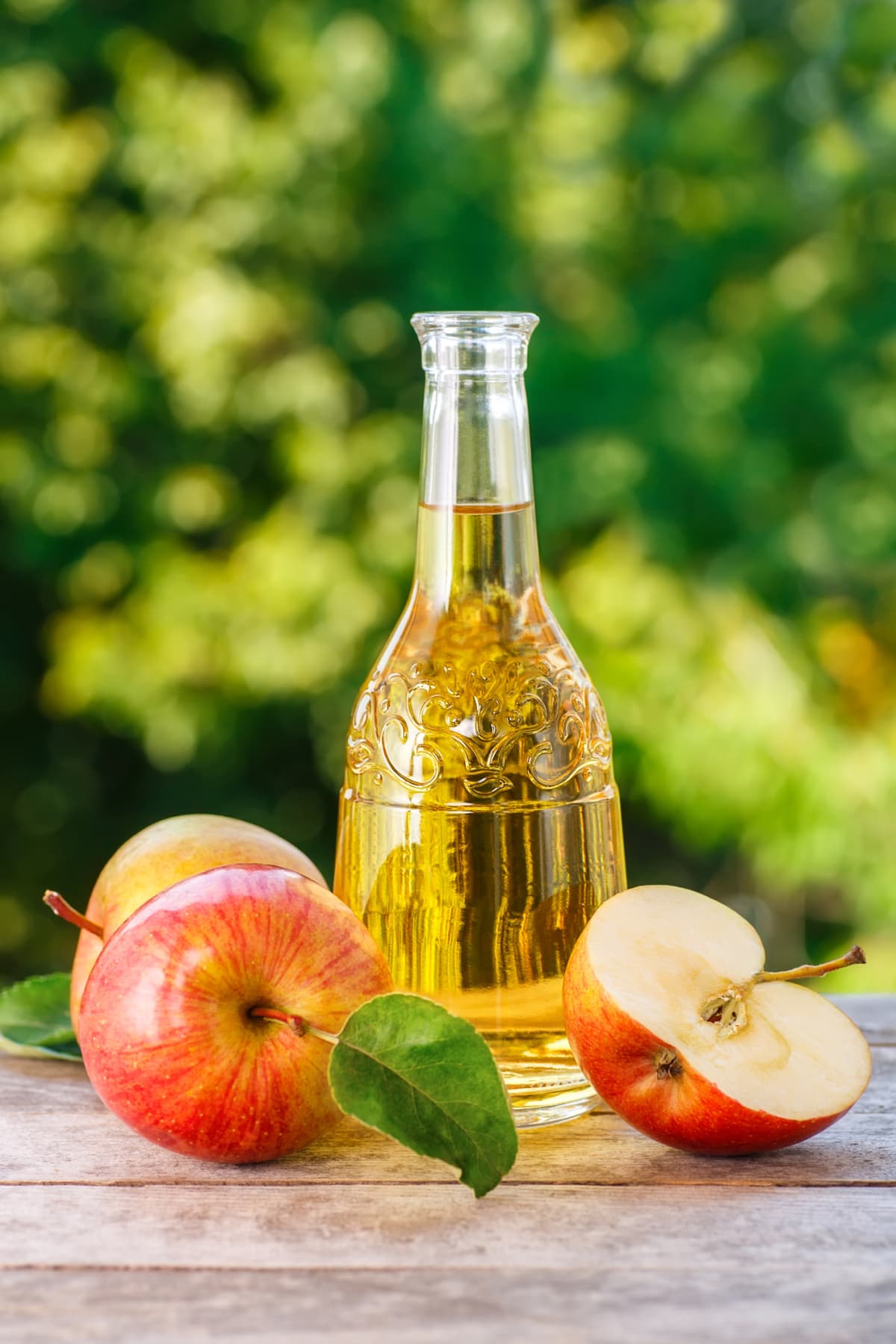 A bottle of apple cider surrounded by red apples