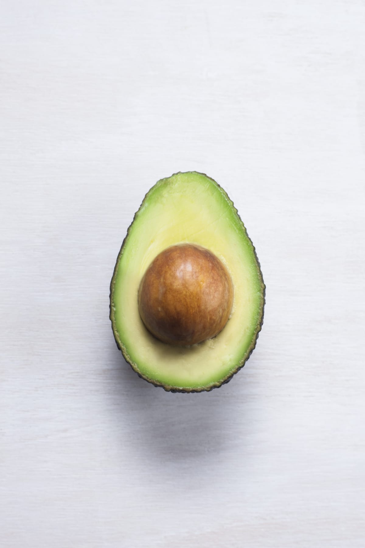 An avocado cut in half. Avocado is the fruit of the avocado tree (Persea americana). The stone is the seed.