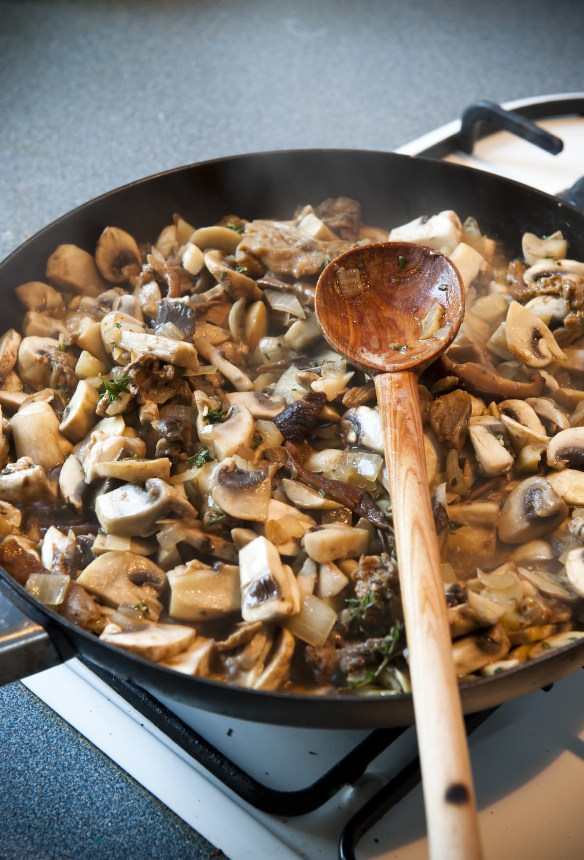 Mushrooms cooking in frying pan on gas stove. Wooden spoon is seen resting in mushroom sauce.See &#8216;Food and Entertaining&#8217; collection: