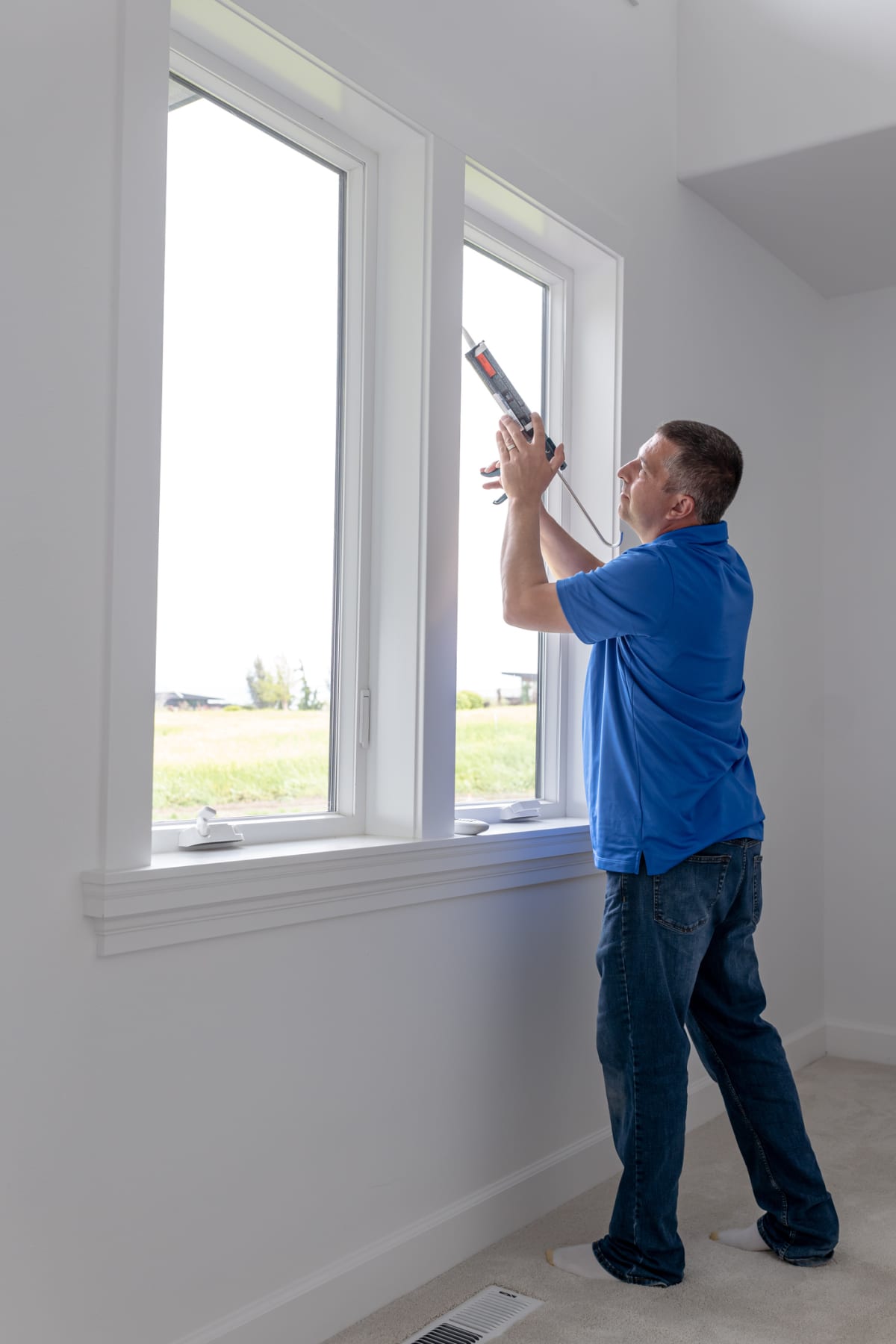 A male homeowner in casual clothing uses a caulk gun when updating his home with new energy efficient windows to make the home more sustainable.