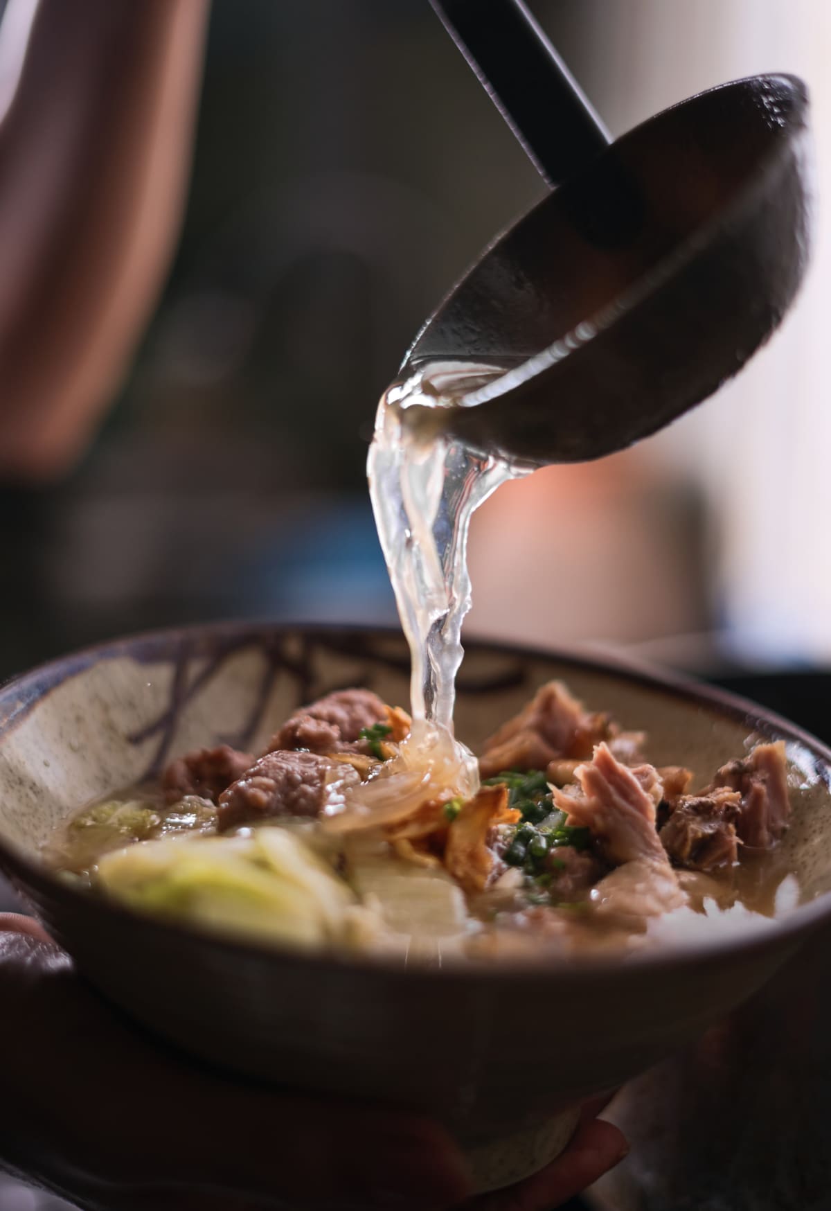A ladle pouring broth into a bowl of beef and noodles