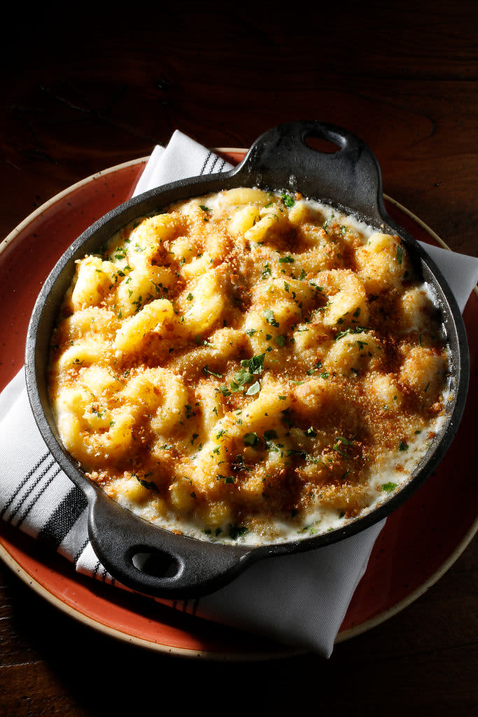 Classic american dish baked mac and cheese in cast iron pan with kitchen towel and ingredients above over old wooden background. Flat lay, space. (Photo by: Natasha Breen/REDA&CO/Universal Images Group via Getty Images)