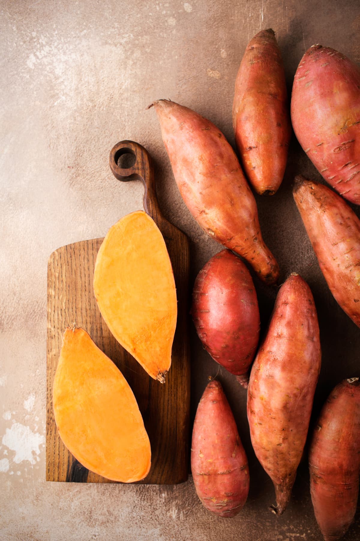 Sweet potatoes on counter with halved sweet potato on cutting board