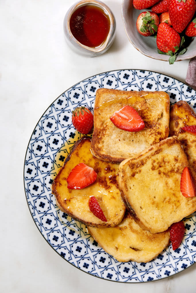 Stockpile of french toasts with fresh strawberries on ceramic plate and pink cloth napkin over white table. (Photo by: Natasha Breen/REDA&CO/Universal Images Group via Getty Images)
