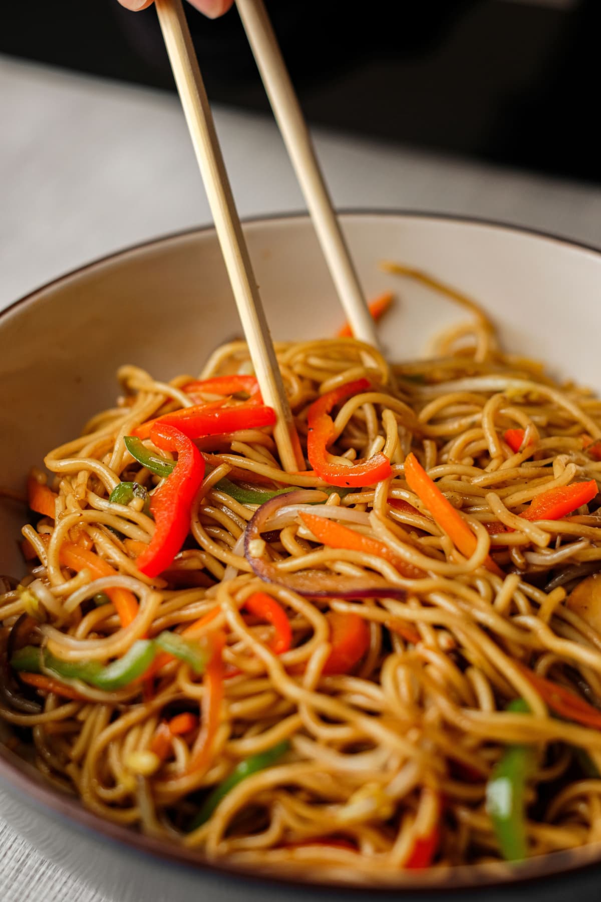 Chow mein, noodles and vegetables dish with wooden chopsticks.