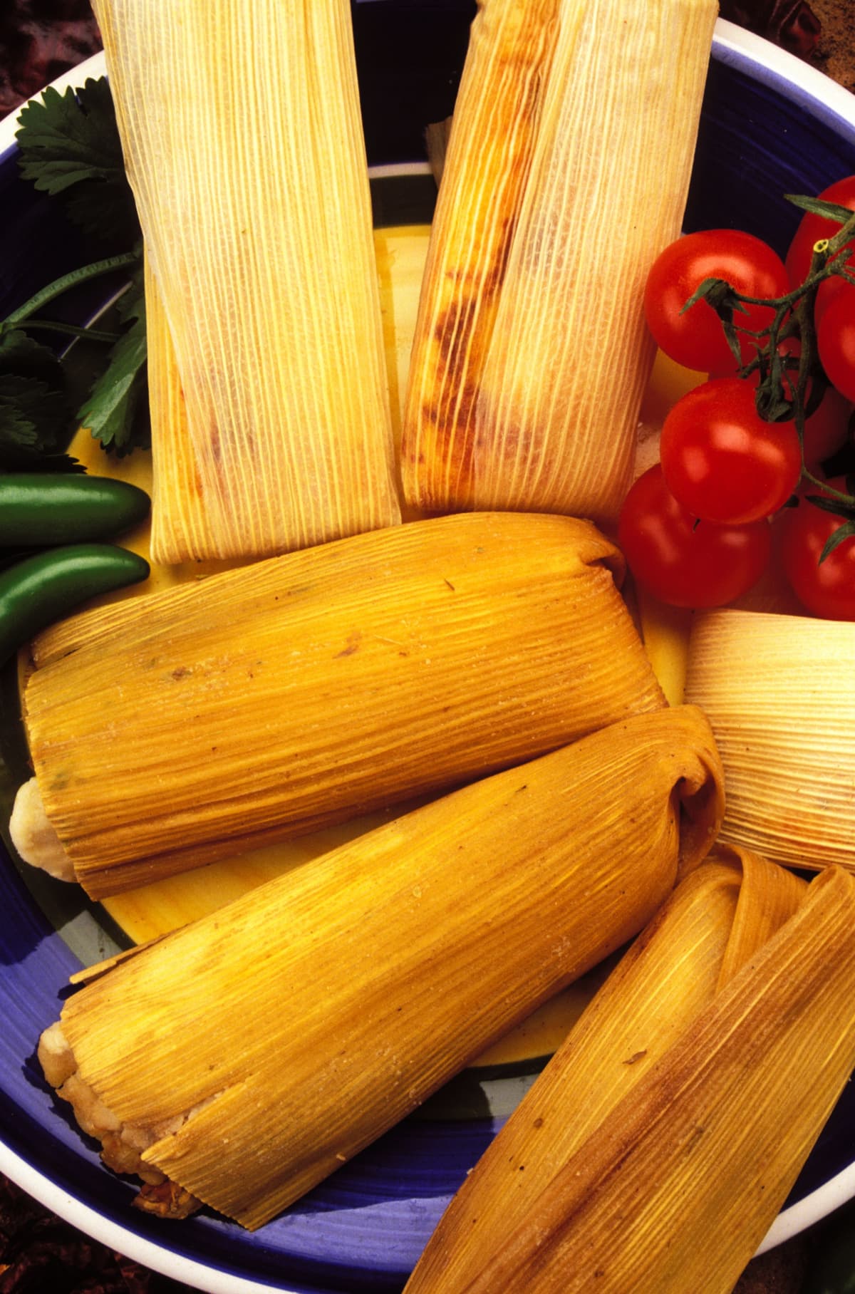 A plate of tamales, tomatoes, and chiles.