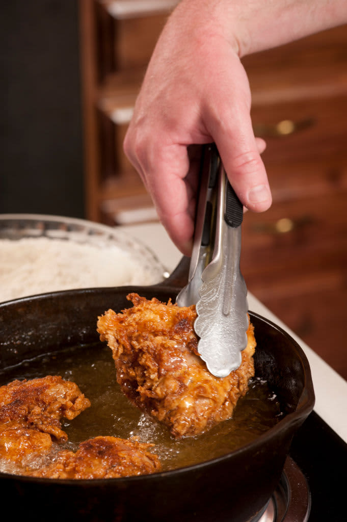 Cook holding fried chicken with tongs