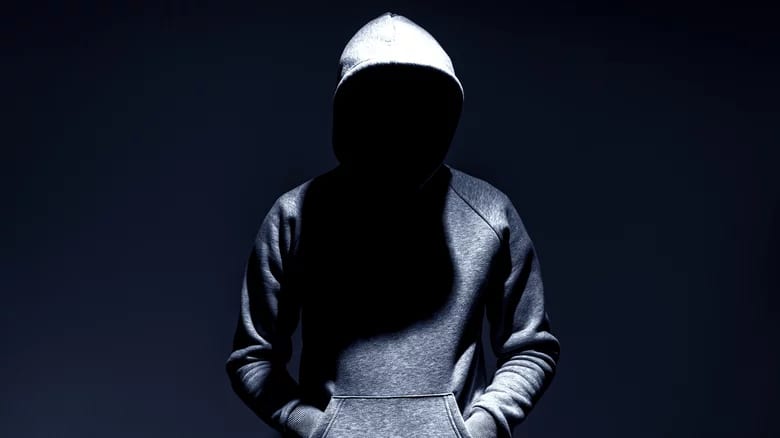 A hooded figure wearing a sweatshirt, the person's face is hidden in shadow.