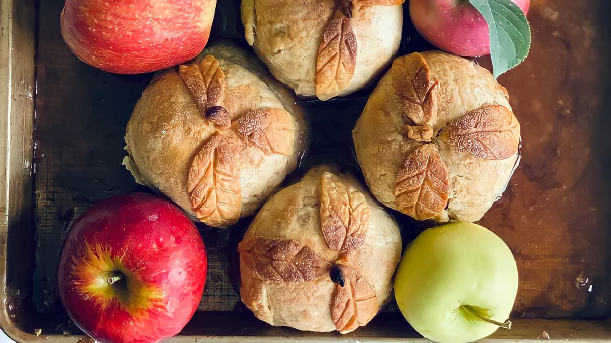 A photo of ornately decorated apple dumplings surrounded by whole apples