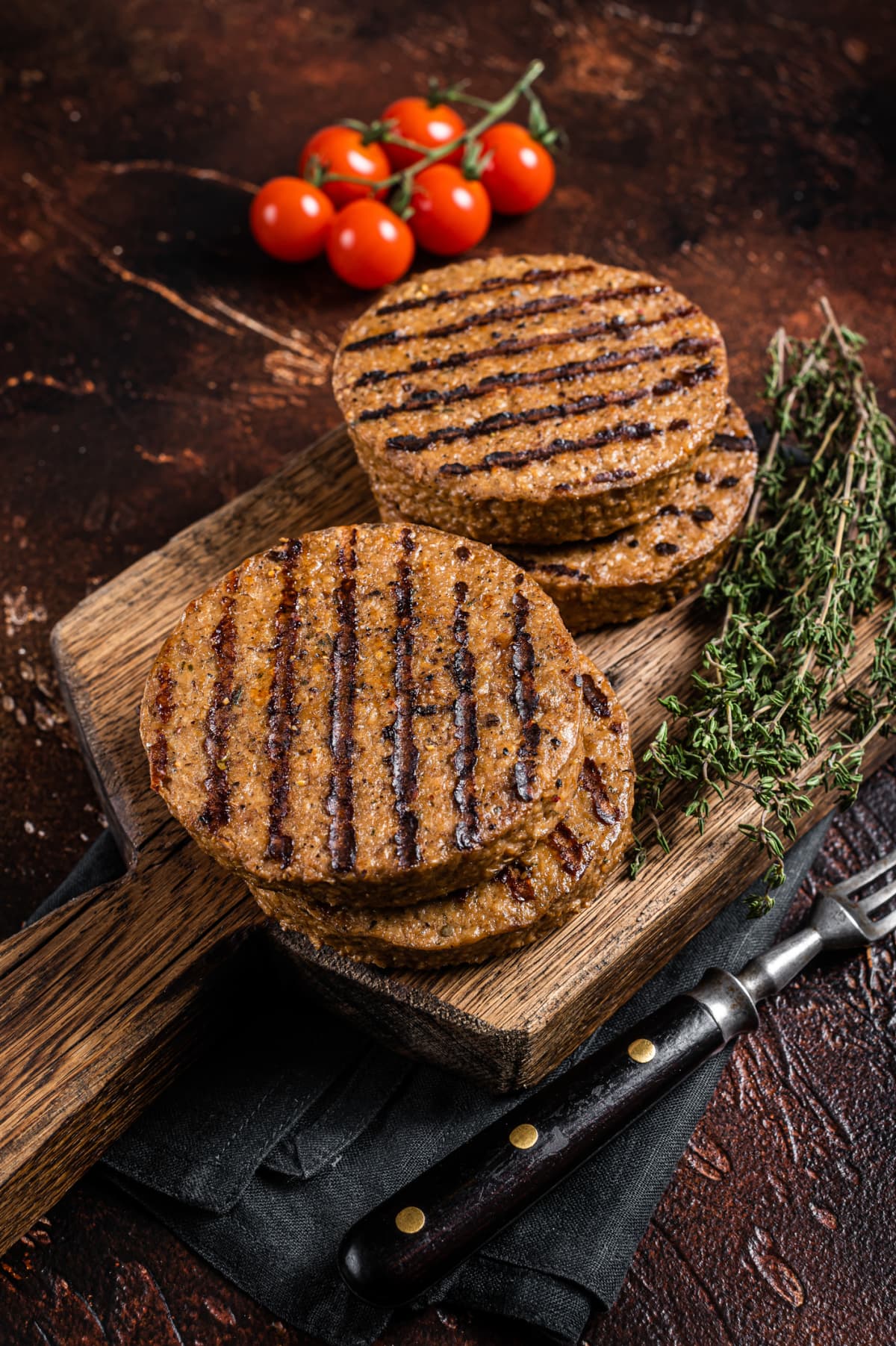 BBQ Grilled plant based meat burger patties,  vegan cutlets on wooden board with herbs. Dark background. Top view.