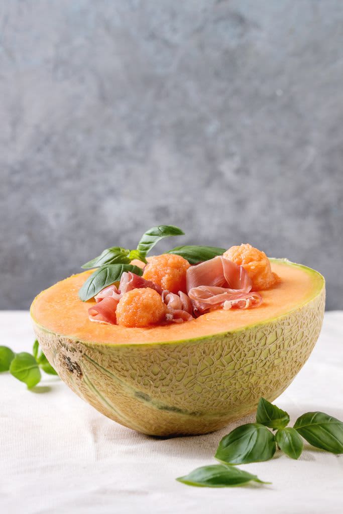 Melon and ham or prosciutto salad served in half of Cantaloupe melon. decorated by fresh basil standing on white tablecloth. . (Photo by: Natasha Breen/REDA&CO/Universal Images Group via Getty Images)