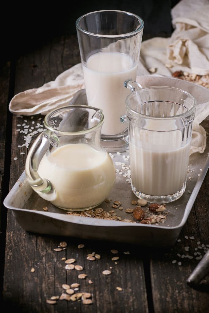 Set of non-dairy milk (rice milk, almond milk and oat milk) in glass cups and jug on old aluminum tray with rice grains, oat flakes and almond over old wooden table. Dark rustic style. (Photo by: Natasha Breen/REDA&CO/Universal Images Group via Getty Images)