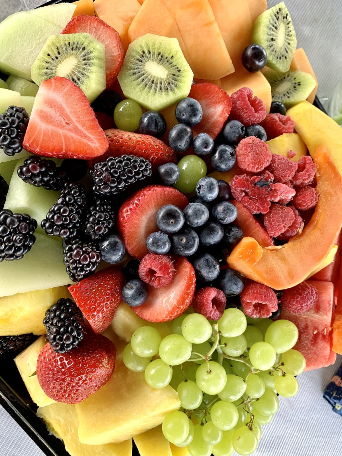 A close up photograph of a beautiful display of fruit salad. Grapes, berries, melon, pineapple & kiwi fill the frame.
