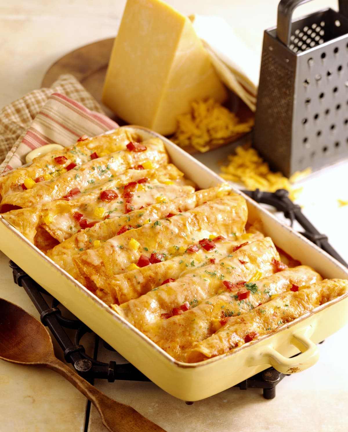 Enchiladas is a baking dish on  a white surface with cheese and a grater in the background