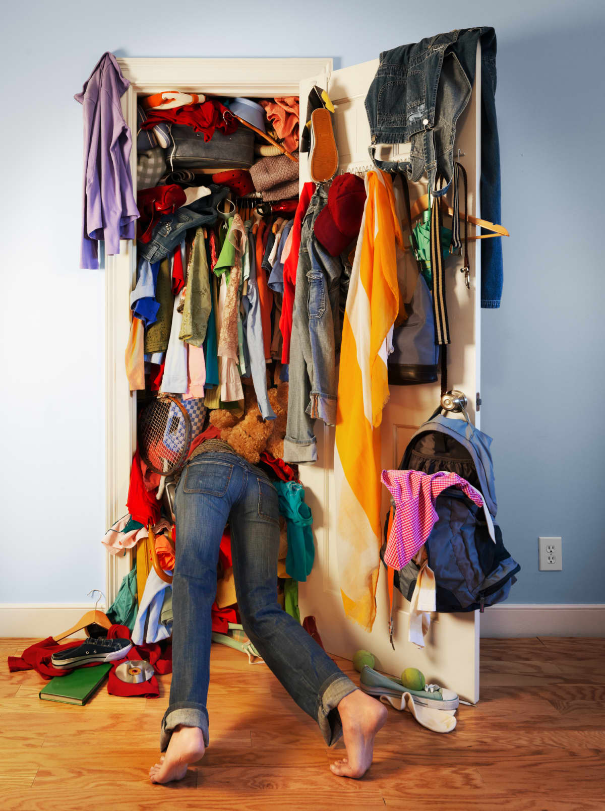 Young woman diving into her very messy, unorganized closet searching for something