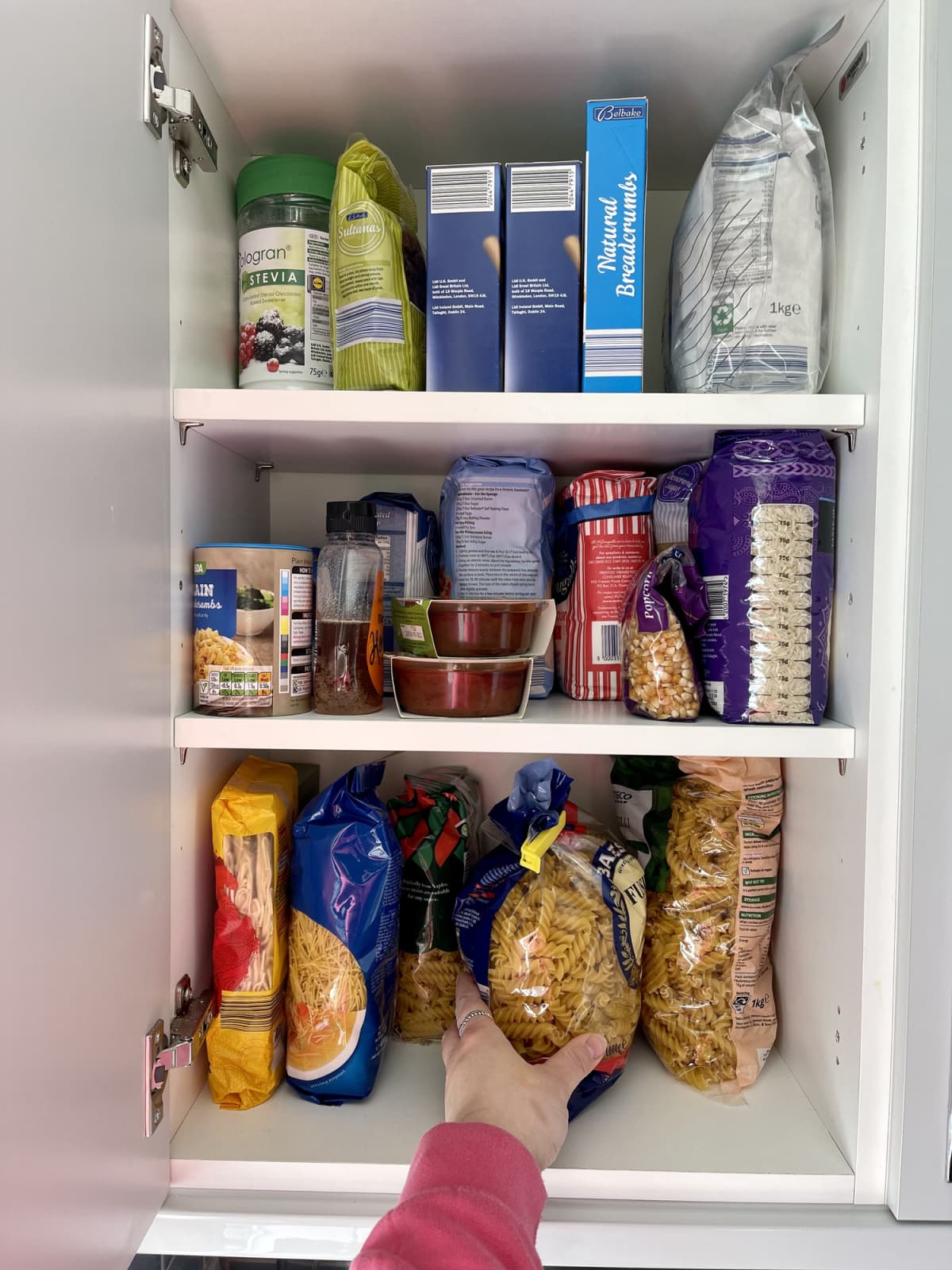 Cabinet stocked with all sorts of dry foods like pasta, noodles, rice, flour, sugar and more
