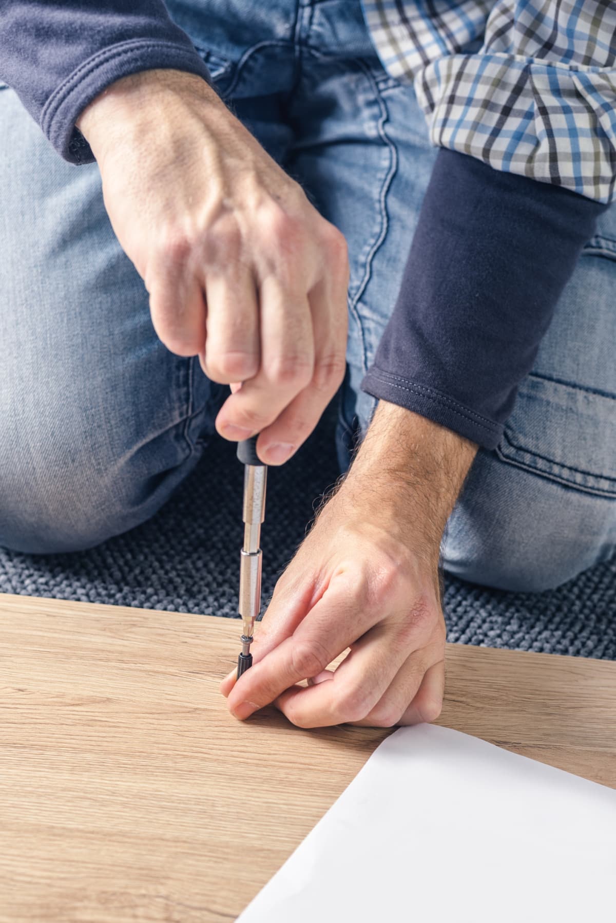 Man assembling furniture at home on the floor, hand with screwdriver