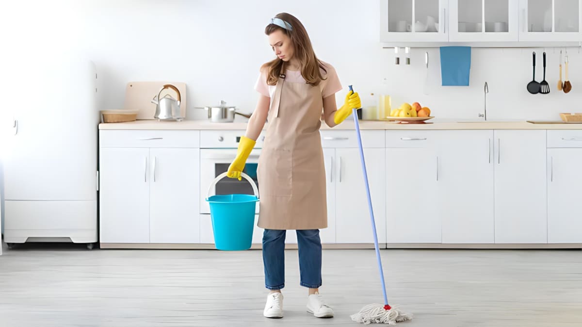 Woman holding mop and bucket in kitchen