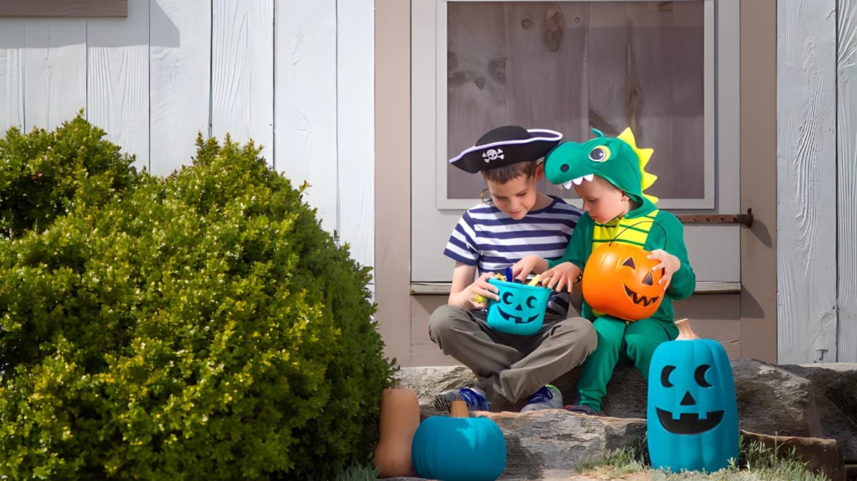 Two children dressed in costumes, looking through a teal pumpkin