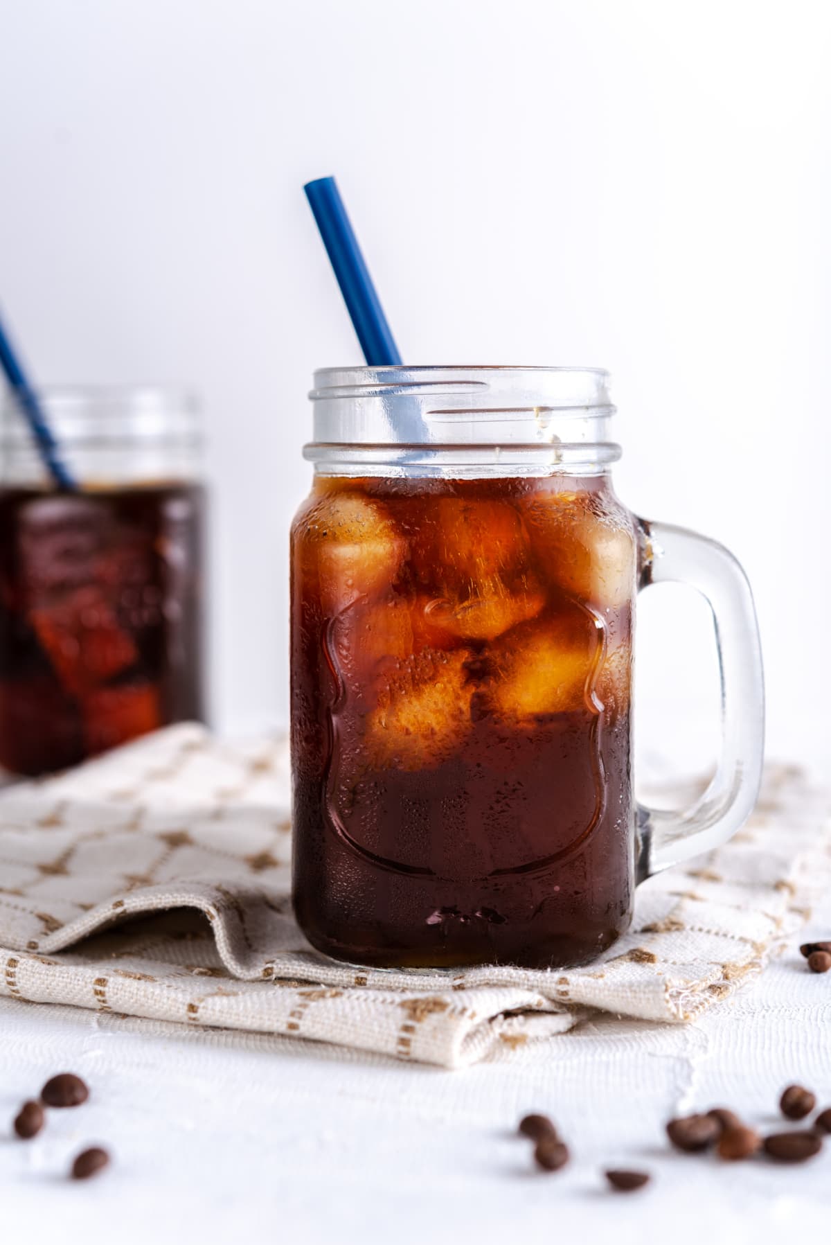 Coffee with ice in a glass mmug with handle on top of cloth napkin with white background