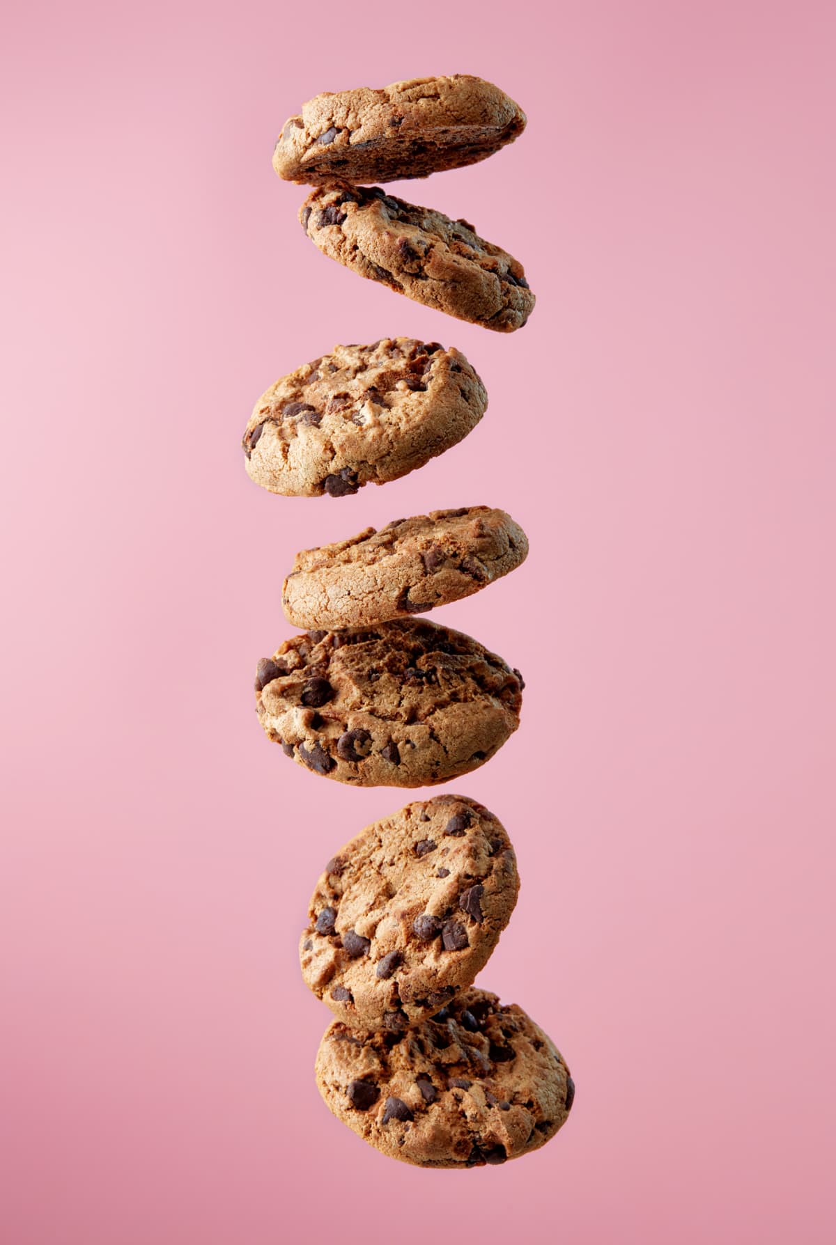 Chocolate chip cookies falling, pink background, food levitation