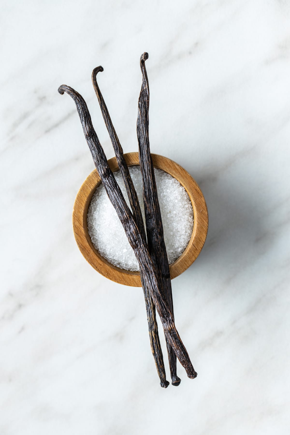 Sticks of vanilla pods resting across the rim of a small wooden bowl of salt