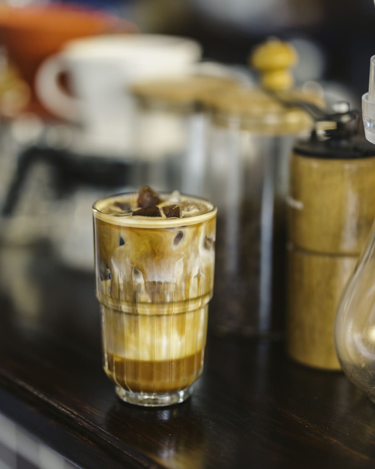 Ice coffee in a tall glass with cream poured over and coffee beans on a grey stone background.