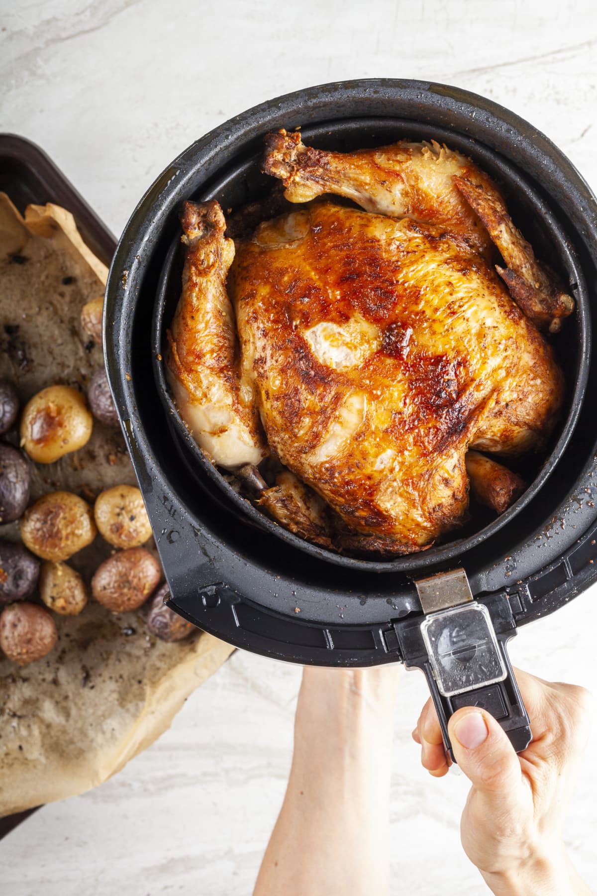 A whole chicken cooked inside an air frier concept. A healthy nutritious homemade alternative to deep fried store bought meat. Served inside the fryers basket together with baked potatoes.