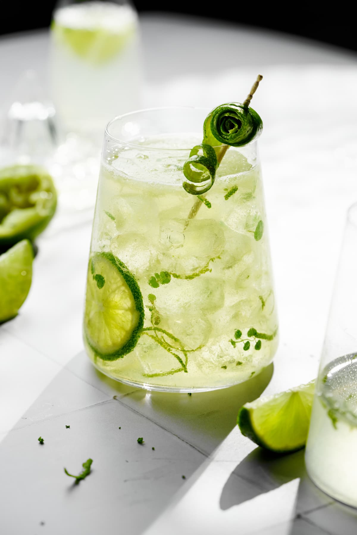 Caipirinha cocktail with lime and cucumber garnishes on wooden table.