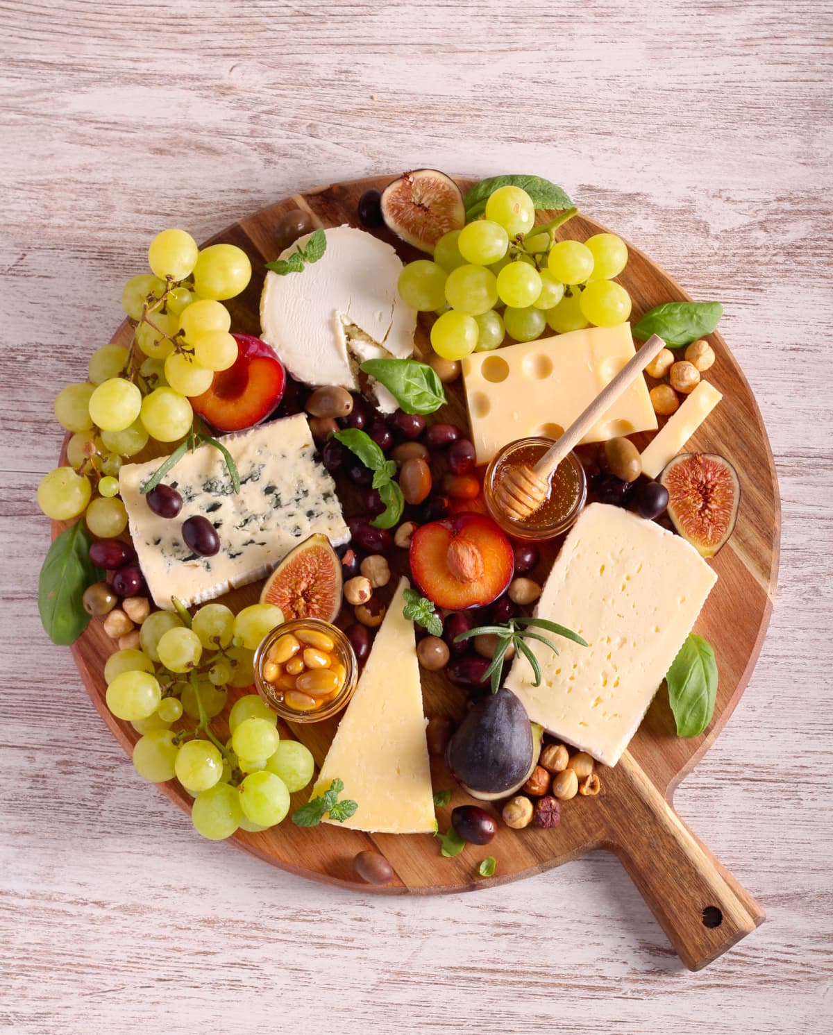 Cheese plate served with red wine, olives, grapes, jam and bread snacks on dark wooden background. Top view.