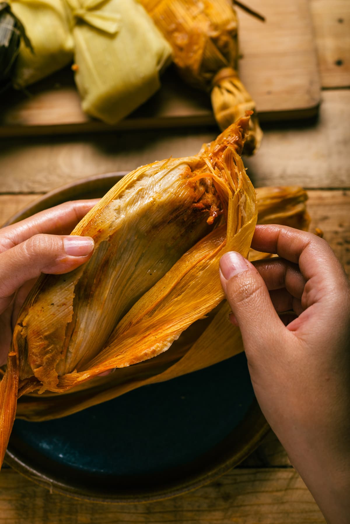 Two hands unwrapping a tamale from its corn husk