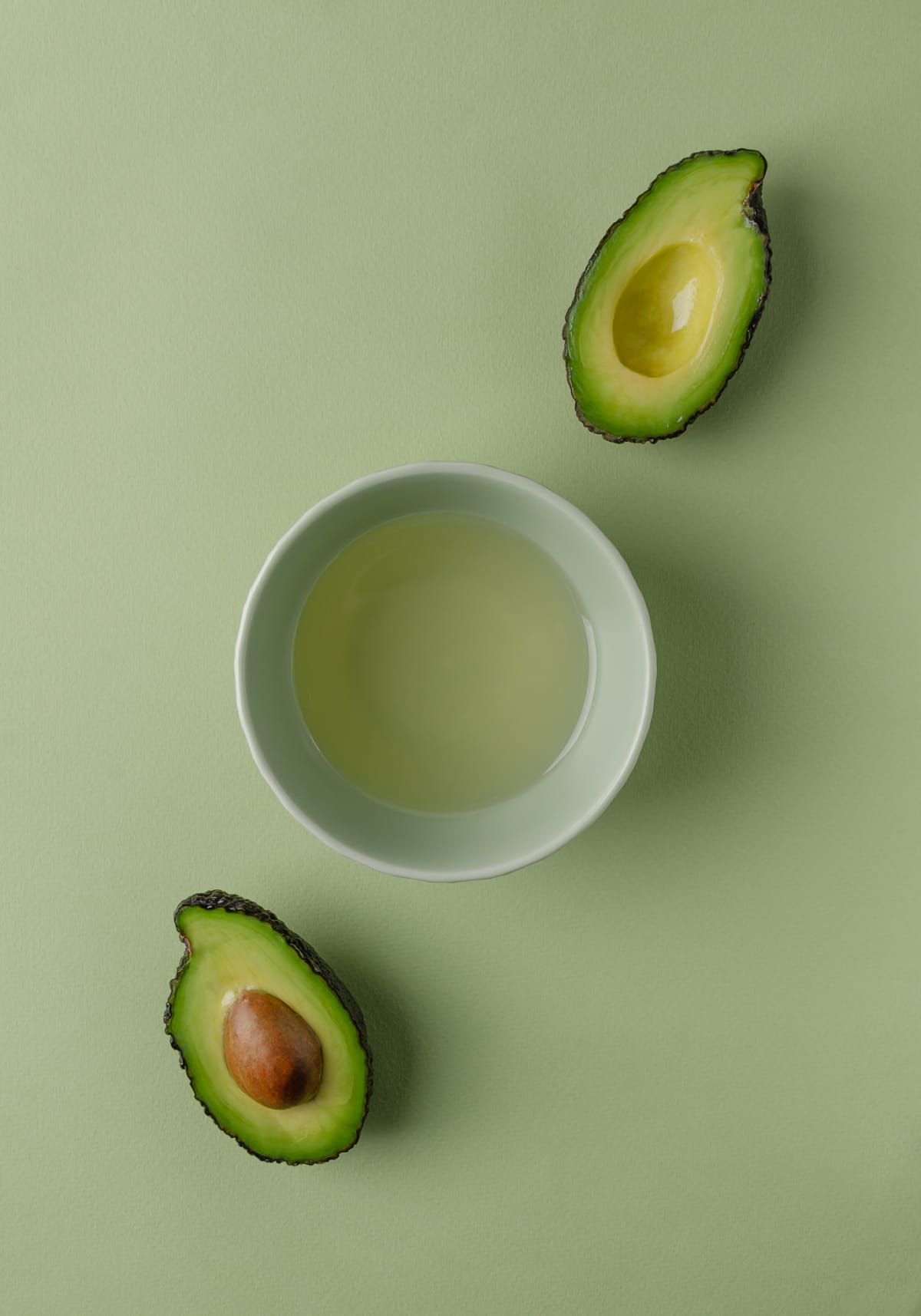An avocado cu in half with each half on either side of a bowl of oil 