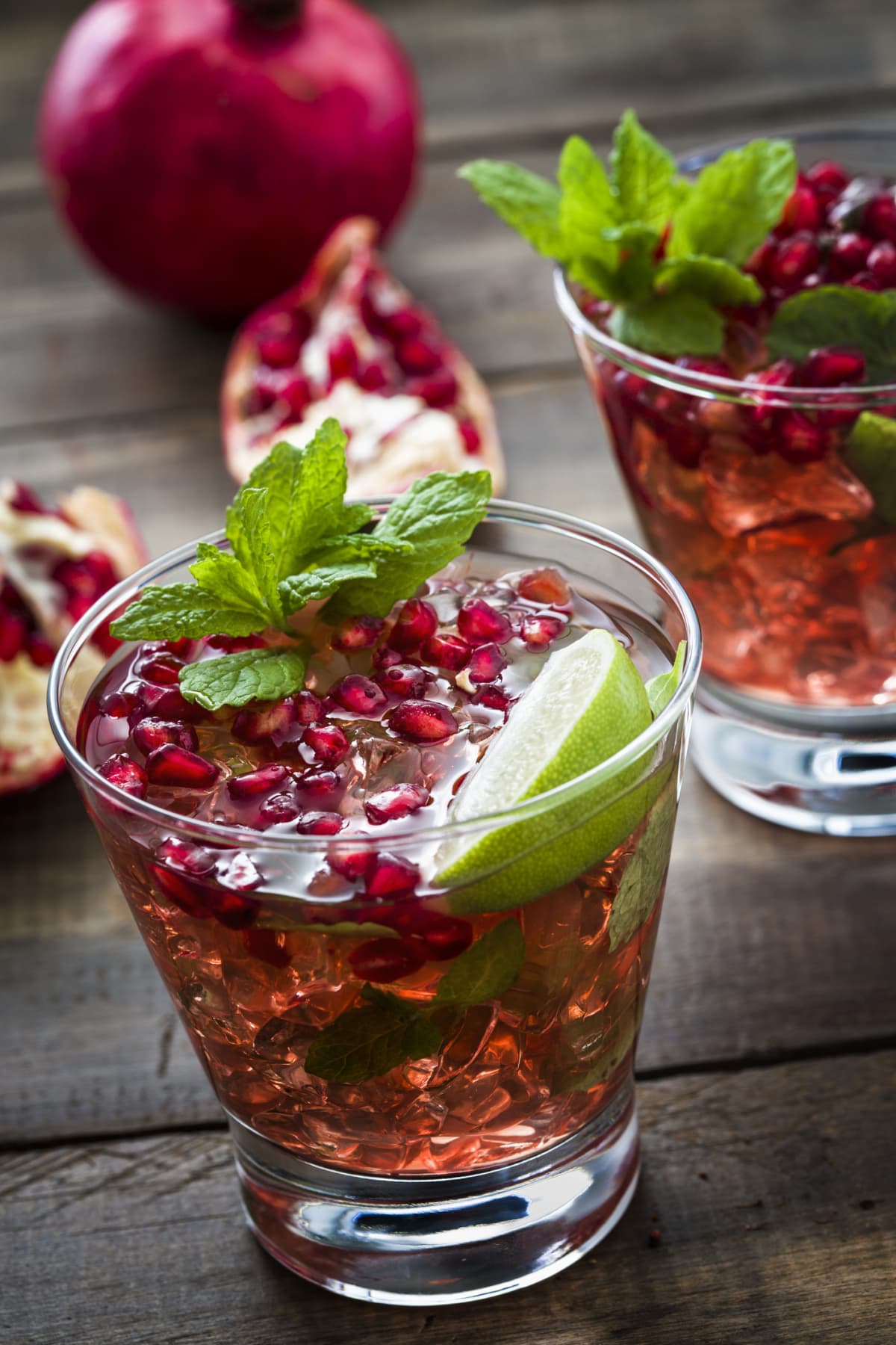 Glass of pomegranate spritzer cocktail with rosemary on green background