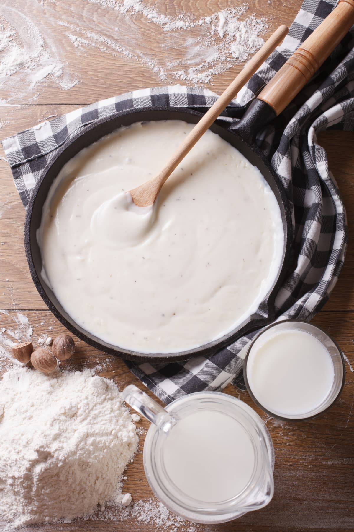 Roux sauce in a pan with a wooden spoon with flour and milk on the side