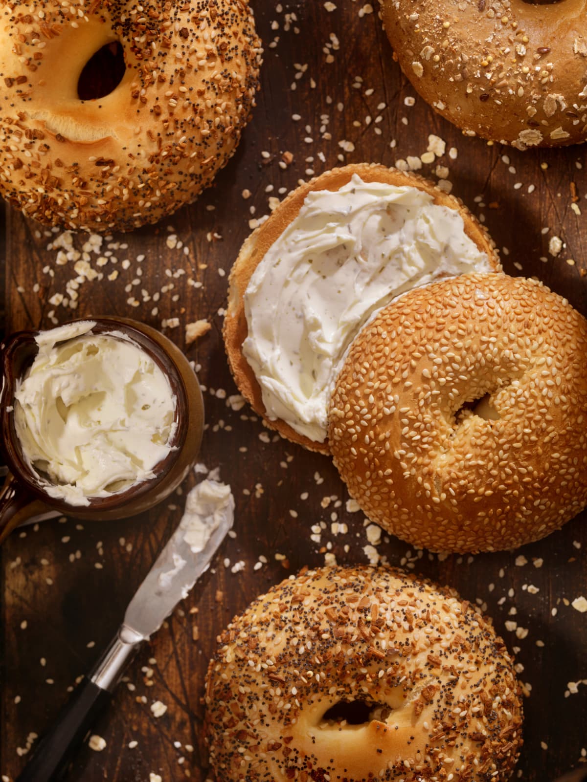 Toasted bagels with cream cheese and a knife on wooden surface