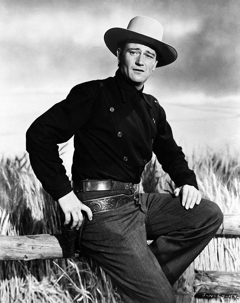 John Wayne (1907 - 1979), US actor, wearing a black cowboy hat and a white neckerchief, holding a rifle in a studio portrait, against a white background, issued as publicity for the film, 'The Searchers', USA, 1956. The Western, directed by John Ford (1894-1973), starred Wayne as 'Ethan Edwards'. (Photo by Silver Screen Collection/Getty Images)