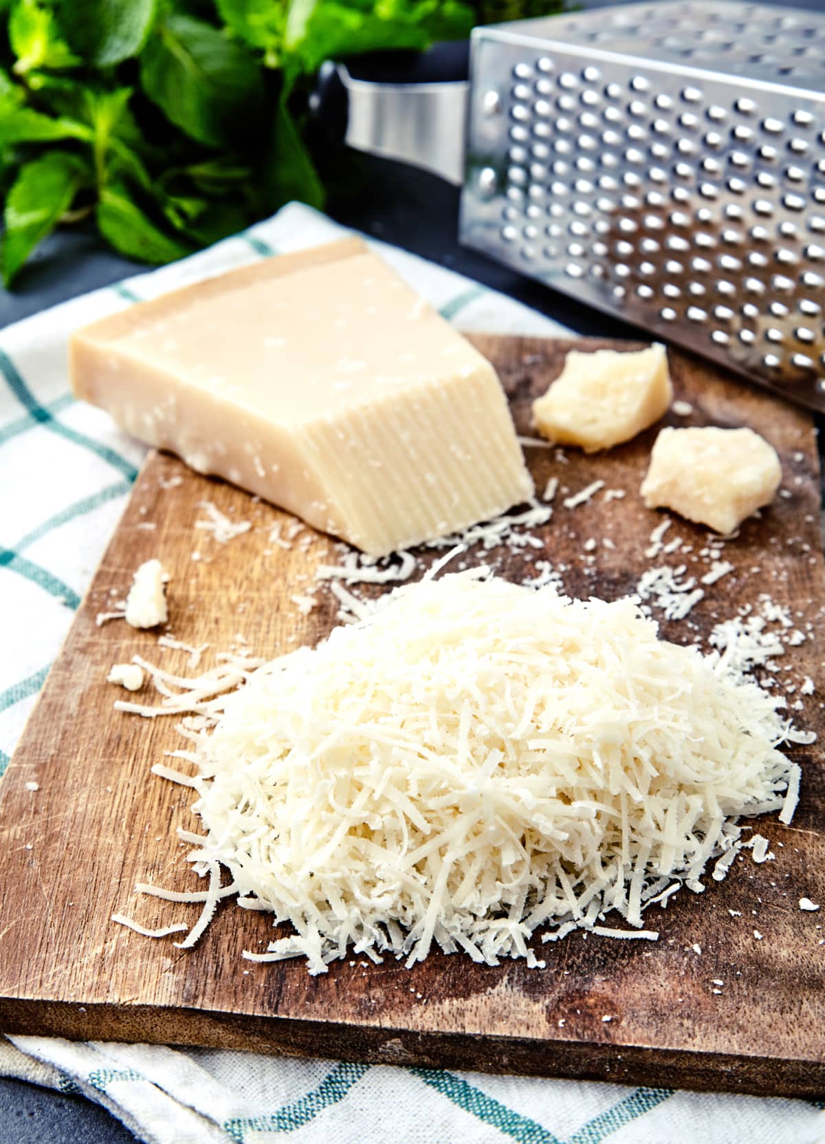 Piece and grated parmigiano reggiano or parmesan cheese on wwood board on checkered napkin . Grated parmesan uses in pasta dishes, soups, risottos and grated over salads.