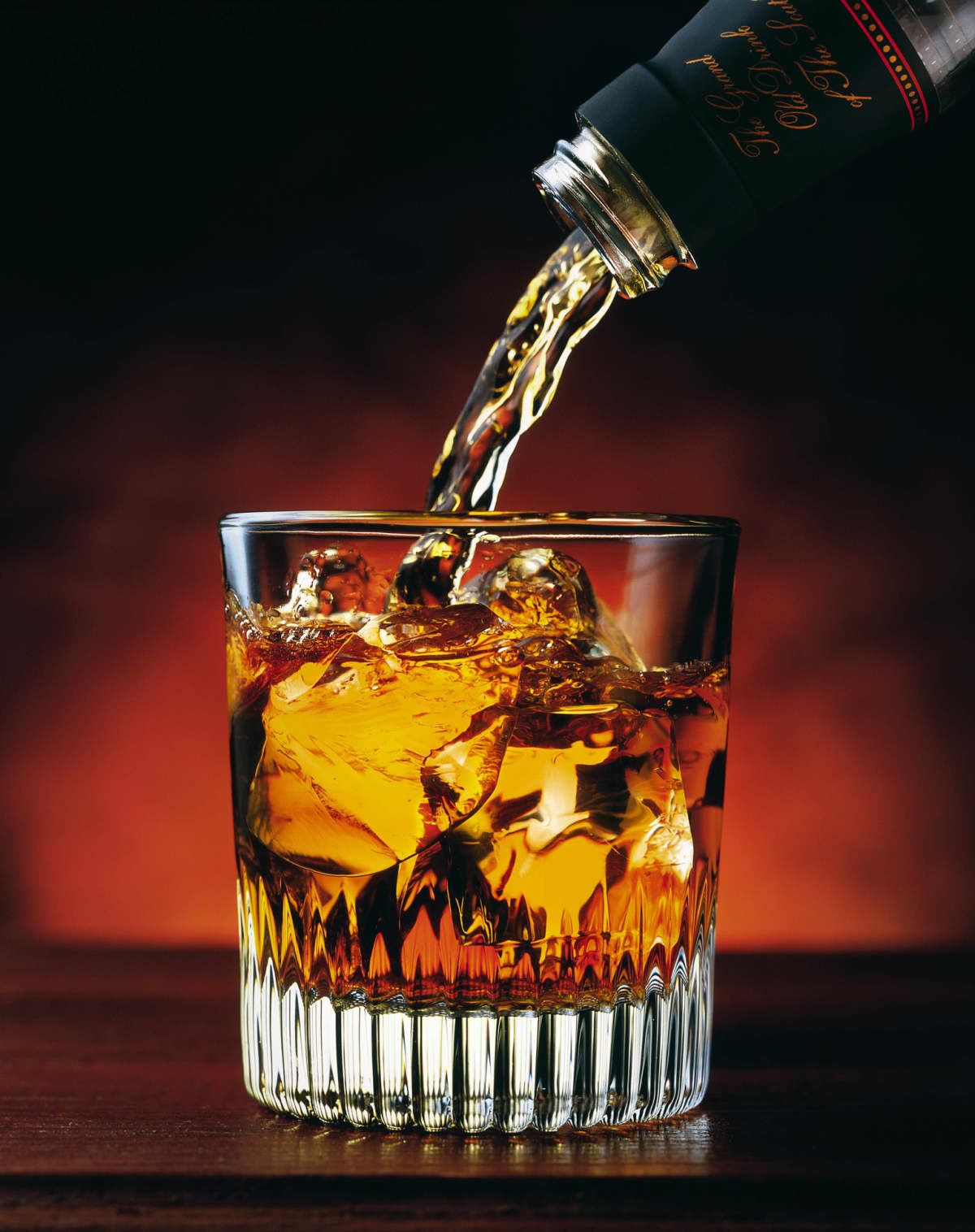 Pouring a glass of whisky with ice from a decanter, in a dark background.