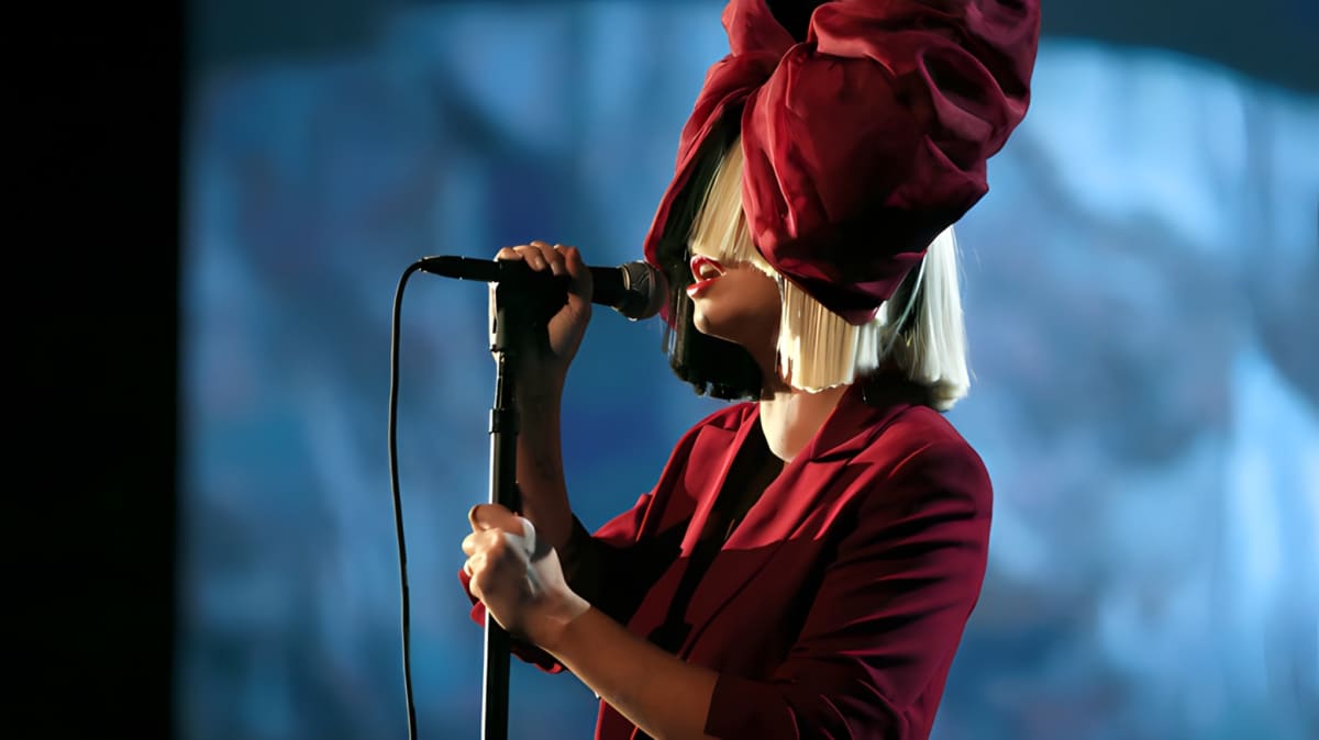 Sia singing into a mic while wearing her wig.