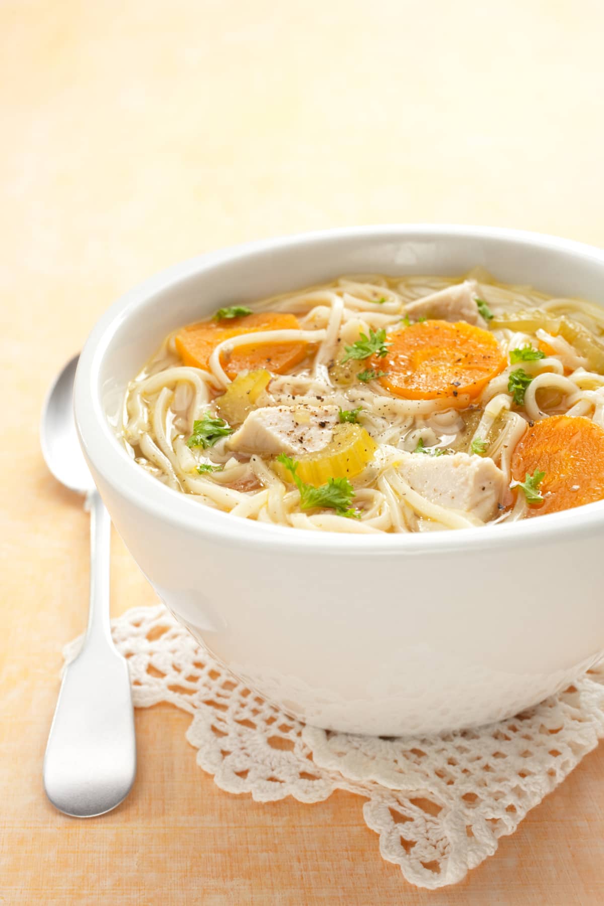 Traditional chicken noodle soup on a pale orange background and a lace mat. More soup:-