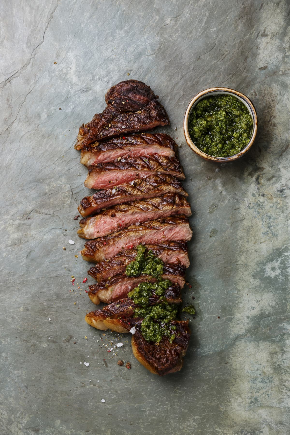 Sliced grilled beef barbecue Striploin steak with chimichurri sauce on gray stone slate background