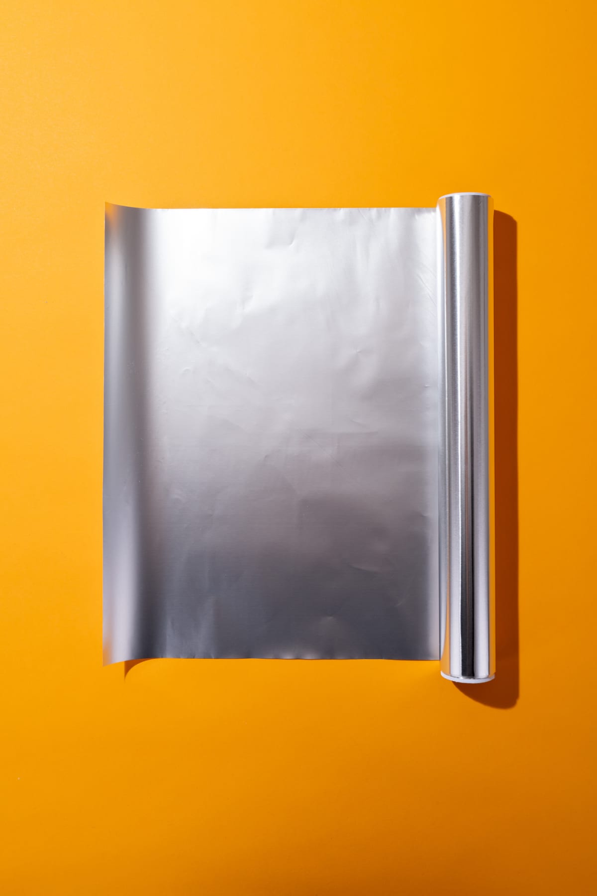 A roll of shiny aluminum foil displayed against a vibrant yellow background