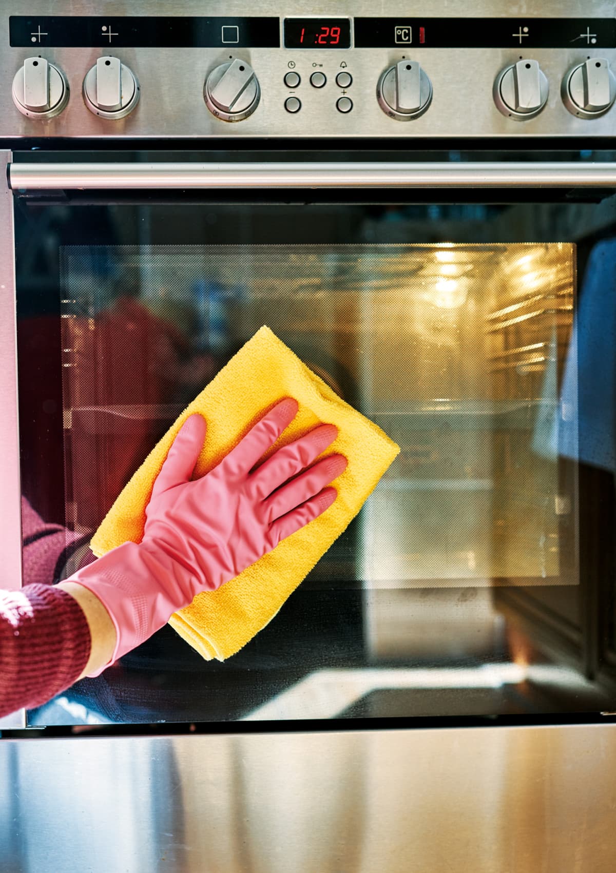 A gloved hand wiping an oven with a yellow rag.
