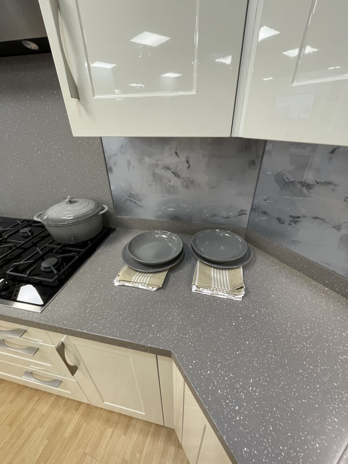 Stock photo showing a black, glass ceramic gas stove top in a grey kitchen counter over glossy, cream floor cabinets.