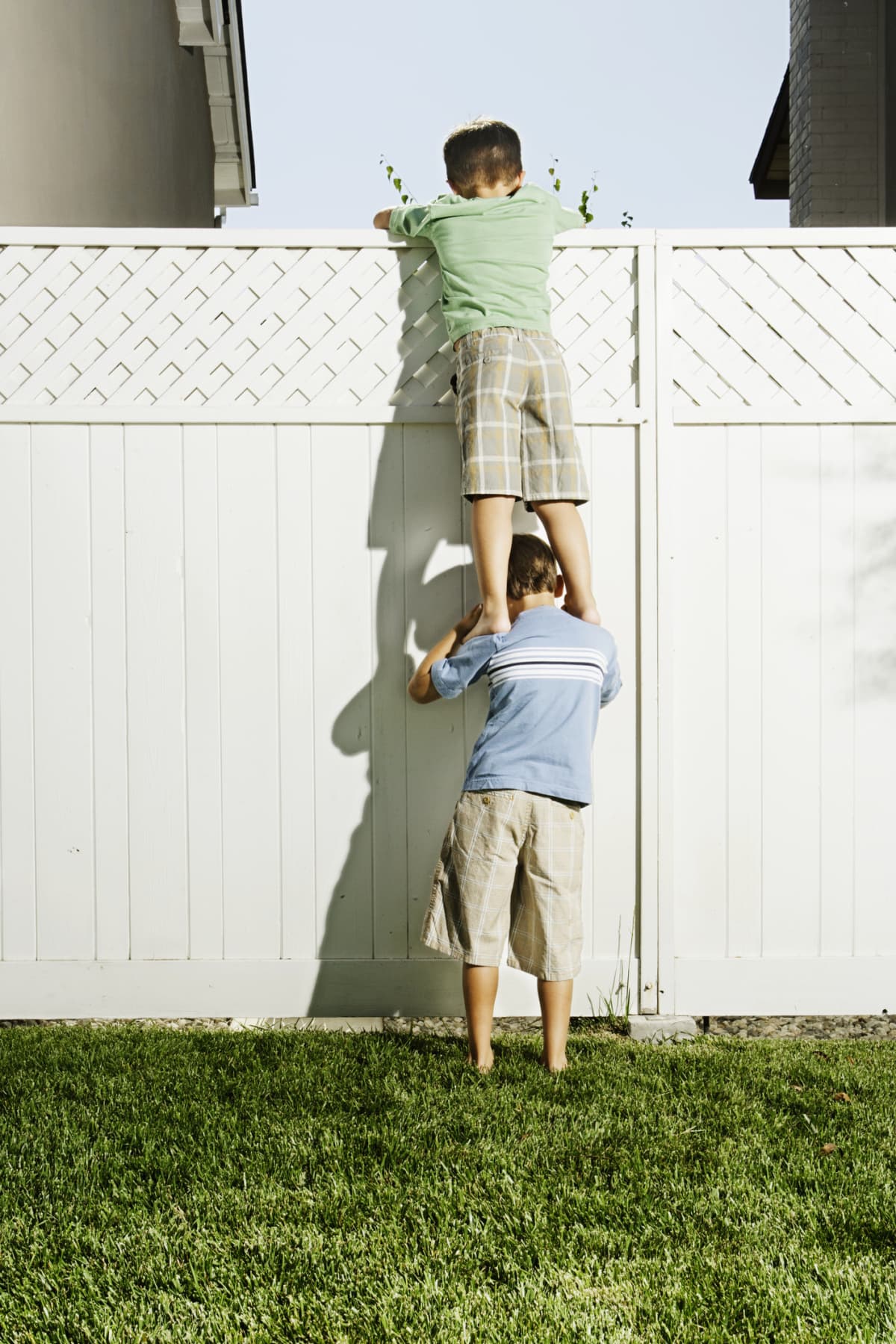 Two boys climbing over white privacy fence in yard