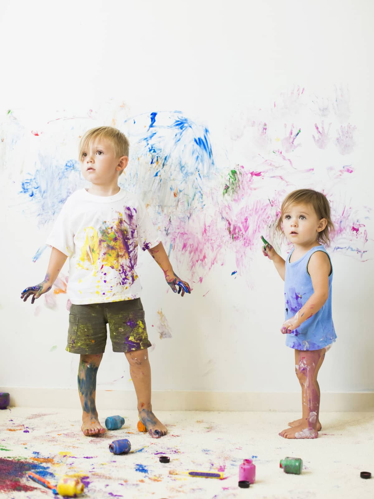 Paint-covered children painting on wall