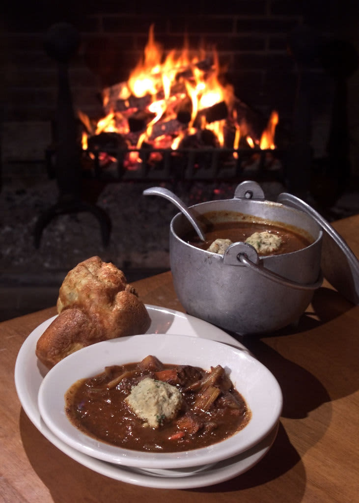 A pot of stew on a table besides a fireplace