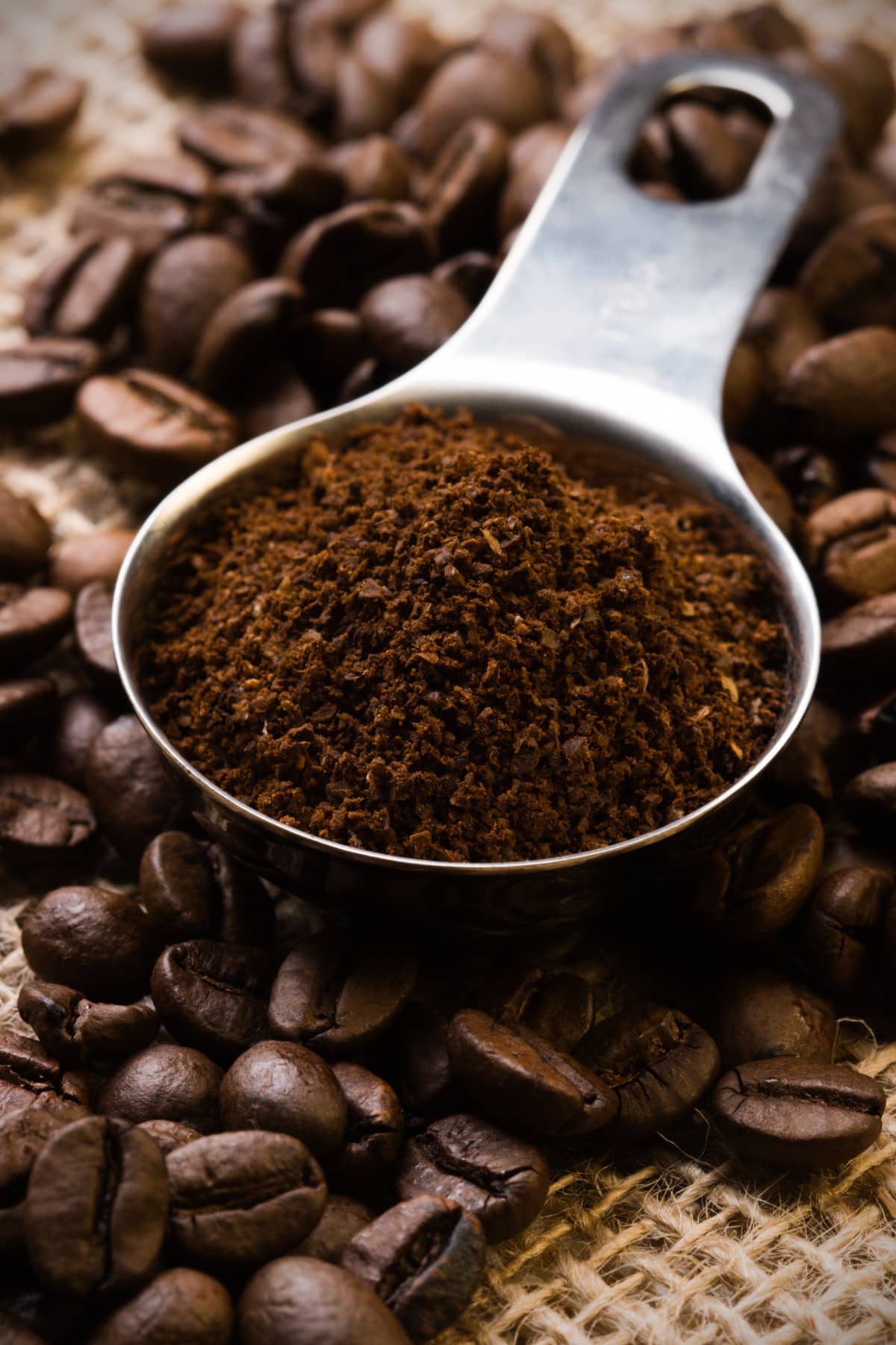 Measuring spoon of ground coffee on top of coffee beans