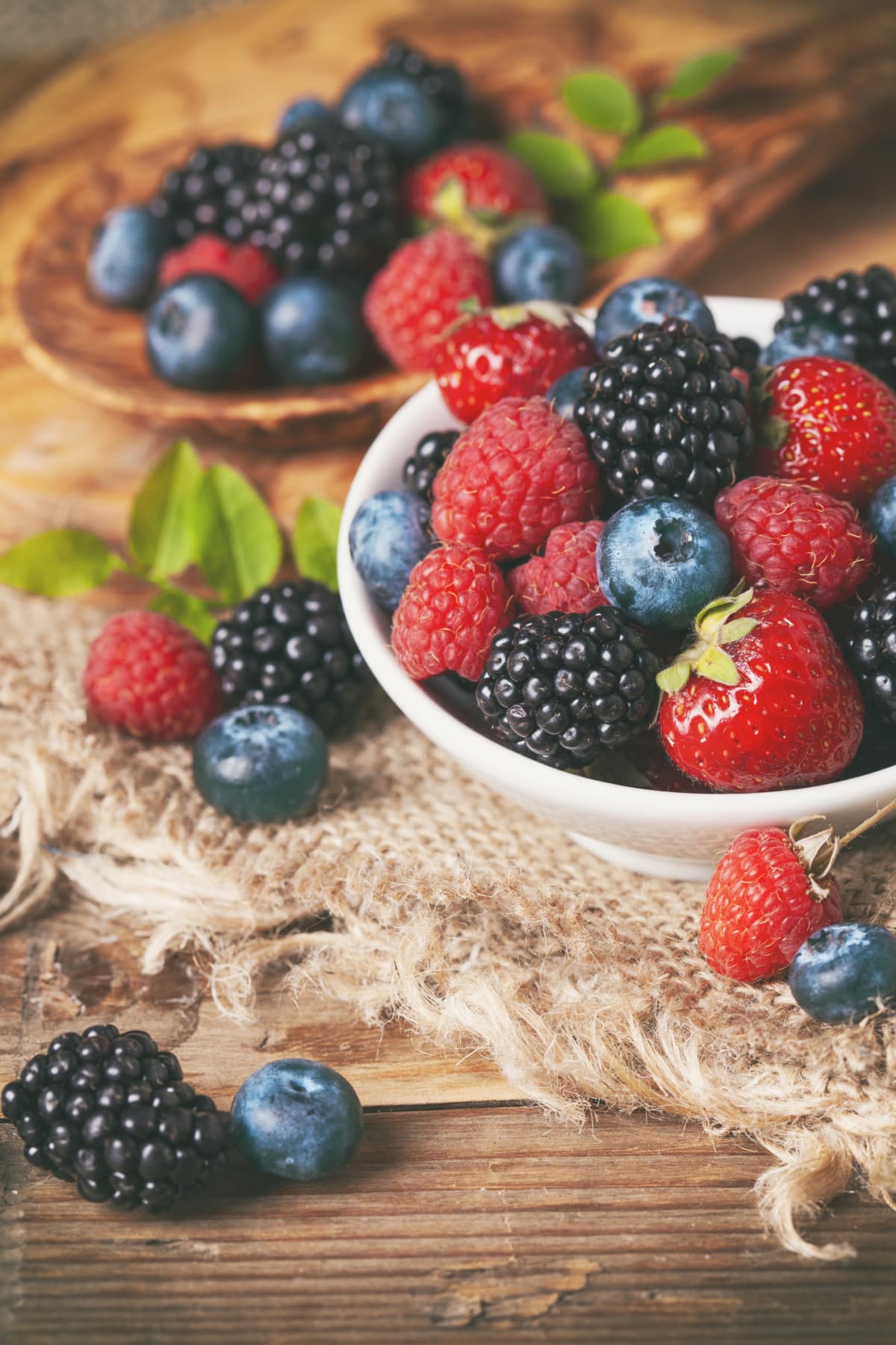 Fresh berries in a bowl and spread around on rustic wooden background