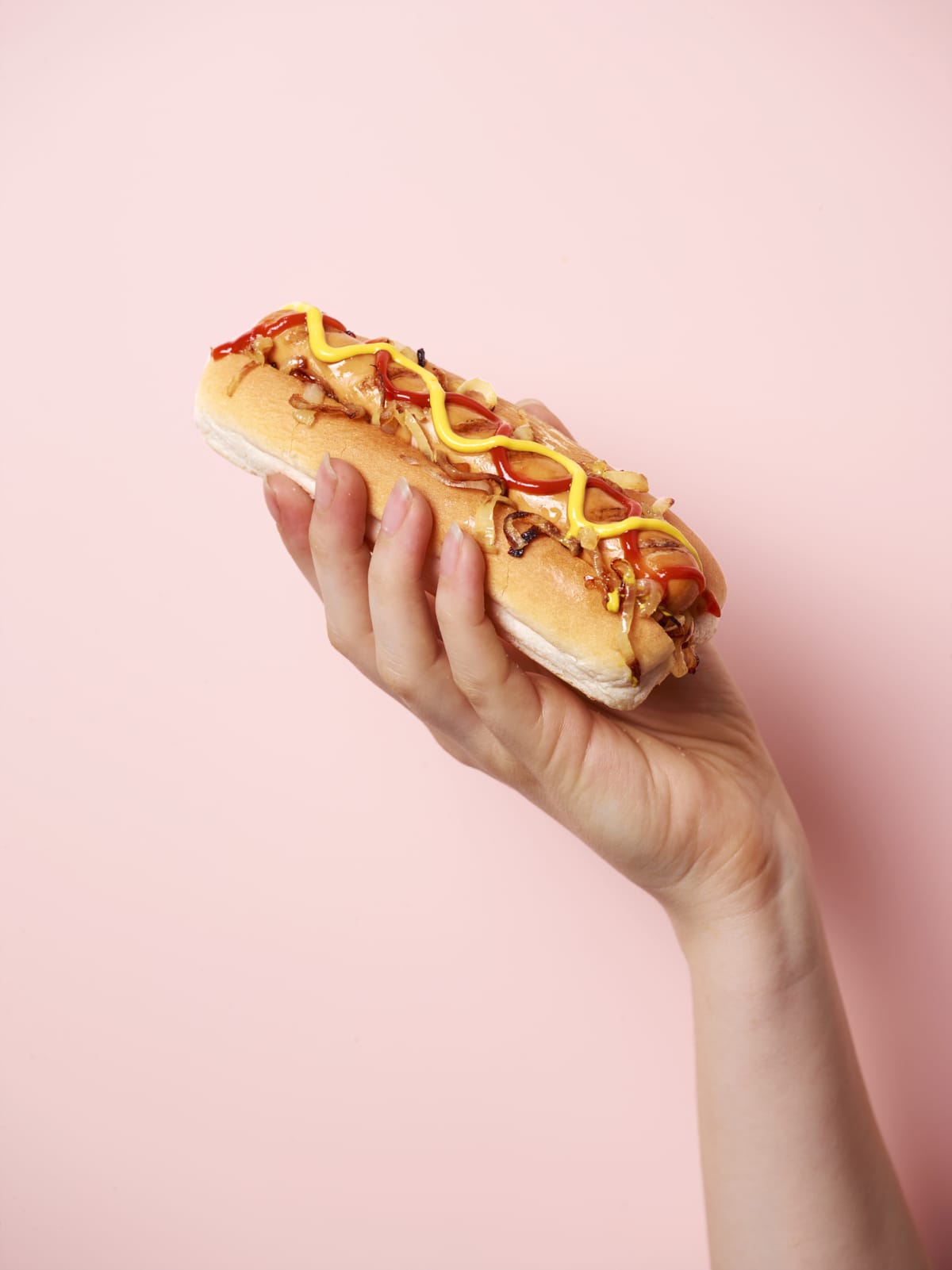 Young female hand holding American style hotdog on a pastel pink background